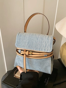 Vintage denim handbag with brown leather straps and gold buckles in a lifestyle setting