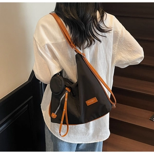 Side view of black nylon tote bag with brown leather straps and small coin pouch detail