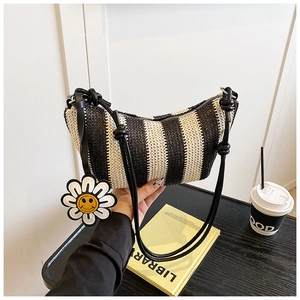 Close-up of a striped woven hobo bag with black leather straps and a smiley flower charm
