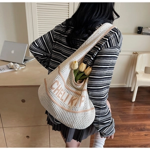 Close-up of beige knit shoulder bag featuring brown embroidered text and woven texture