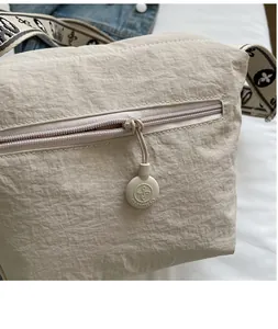 Close-up of smooth zipper on beige nylon crossbody bag with metallic brand pendant