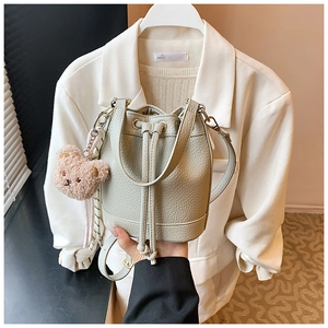 Green bucket bag with lychee texture and pink bear charm shown in a hand-held pose