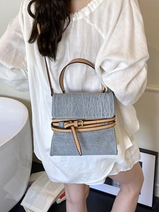 Blue denim crossbody handbag with brown leather trim and metal buckle detail on model