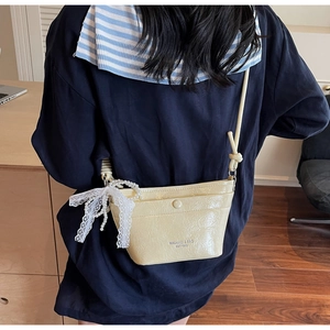 Detail of beige patent leather bucket bag with white lace bow and pearl charms decoration