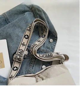 Detail of wide jacquard shoulder strap with floral logo on beige canvas crossbody bag