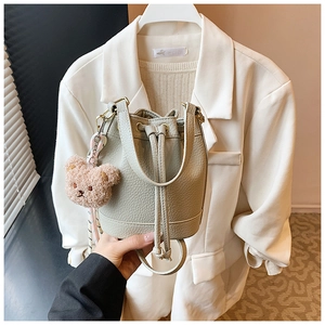 Detail of mint green pebble leather bucket bag with drawstring and pink plush bear charm