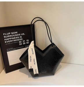 Detail of glossy wrinkled leather shoulder bag with decorative ribbon and metal nameplate