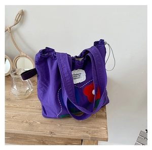 Detail of purple canvas tote bag with floral patches and drawstring closure