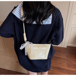 Detail shot of cream crossbody bucket bag with pearl lace bow charm on a model