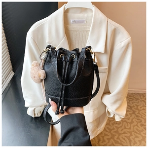 Detail of black pebbled leather bucket bag with gold eyelets and cute plush bear charm