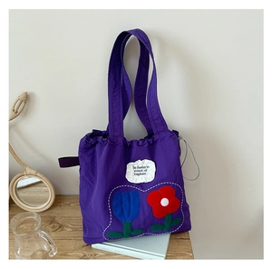 Close-up of purple canvas tote bag with floral embroidery and white patch on wood table