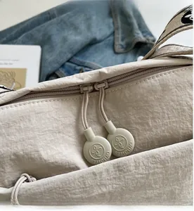 Close-up of smooth double zipper pulls with logo on a beige nylon crossbody bag