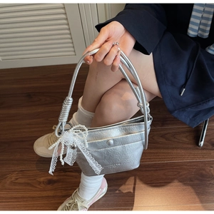 Detail of silver pleated bucket bag featuring pearl lace charm and brand logo