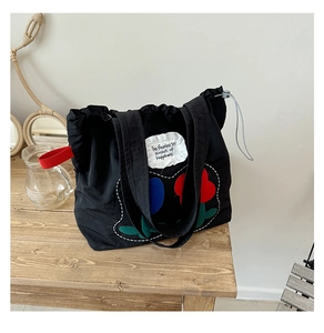 Detail of black canvas tote with floral patches and red webbing handles on wood surface
