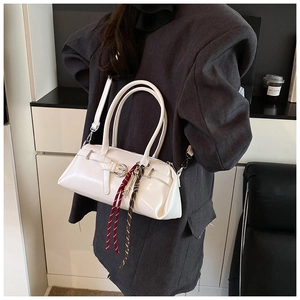 Detail of white glossy Boston bag with buckle decor and woven tassel on grey blazer