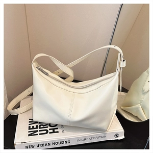 Detail of a creamy white crescent bag with adjustable strap and textured leather finish