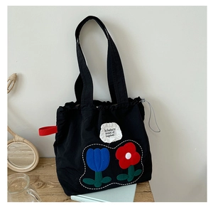 Close-up of black tote bag with floral embroidery and ruffle fabric patch on wood table