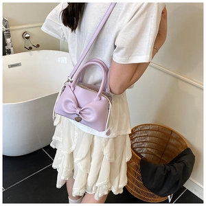 Dettaglio borsa a secchiello lavanda con fiocco in pelle e ciondolo a cuore su modella