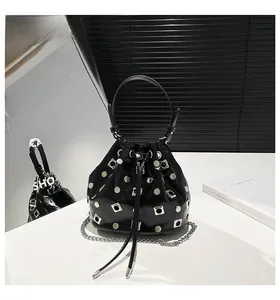Detail of a black glossy leather bucket bag featuring silver metal studs and chain strap