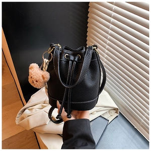 Detail of black pebbled leather bucket bag with white contrast stitching and bear charm