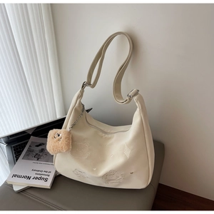 Detail of beige tote bag with cute cat embroidery and plush pendant on a leather bench