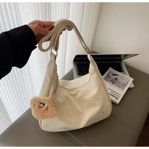 Detail of cream crossbody bag with cat embroidery and plush pendant in lifestyle setting