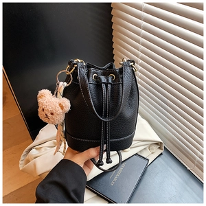 Close-up of black lychee grain bucket bag with teddy bear charm and decorative silk scarf