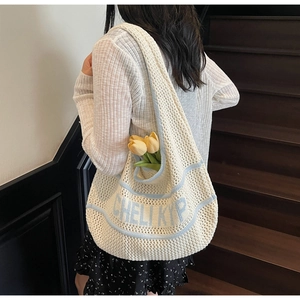 Detail of a cream knit tote bag with blue stripes and text on a wooden staircase