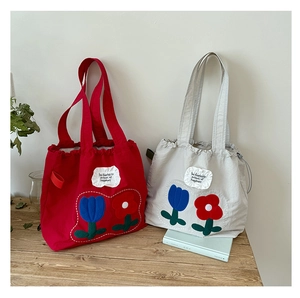 Detail of red and gray canvas tote bags with tulip embroidery and drawstring top closure