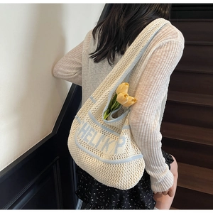 Detail of hand-knit cream tote bag with blue HELIKP lettering and fresh tulips inside