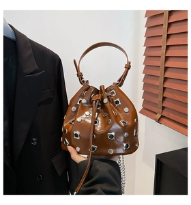 Detail of a brown bucket bag with metallic rivets and shiny finish in a studio setting