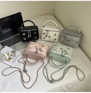 Five elegant box-style bow handbags in various colors displayed with lifestyle props