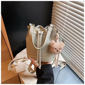 Close-up of beige drawstring bucket bag with lychee texture and cute bear charm