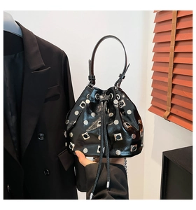 Detail of black patent leather bucket bag featuring silver rivet studs and drawstring closure