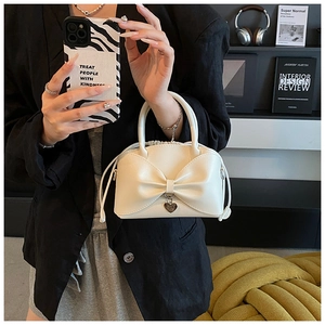 Détail du sac seau blanc crème avec grand nœud et pendentif cœur argenté porté à la main