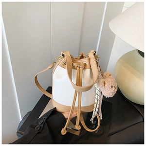 Close-up of a white and khaki bucket bag with drawstring and cute bear accessory