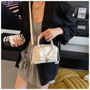 Détails du sac seau crème avec nœud décoratif, pendentif cœur et bandoulière