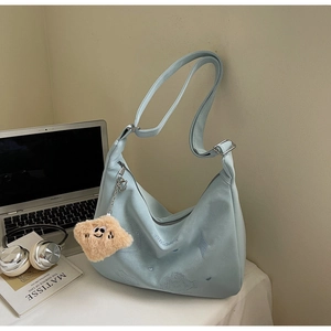 Detail of light blue embroidered crossbody bag with plush charm and laptop on a desk