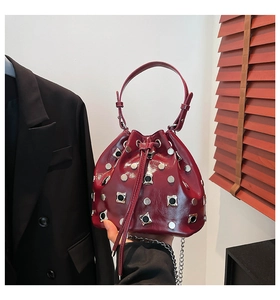 Detail view of burgundy bucket bag with silver rivets and metallic chain strap