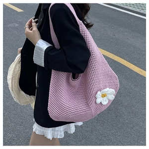 Détail d'un sac à bandoulière tressé rose avec une décoration de marguerite blanche