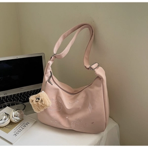 Close-up of pink crossbody bag with cat embroidery and plush pendant on desk