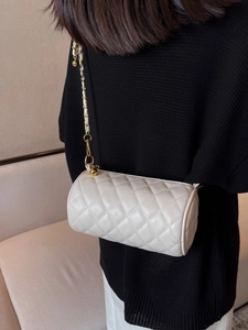 Sac cylindrique blanc matelassé avec bandoulière en chaîne dorée porté par un mannequin