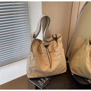 Detail of a large beige crossbody bucket bag with pleated texture and drawstring closure