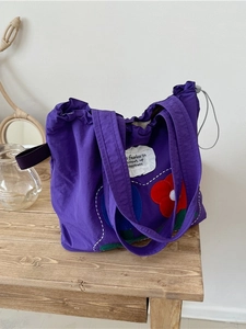 Purple drawstring tote bag with floral patch embroidery on a wooden table setting