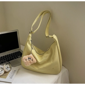 Detail of yellow crossbody bag with embroidery and cute plush charm on a desk