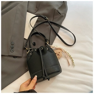 Detail of black lychee grain leather bucket bag with contrast white stitching and charms