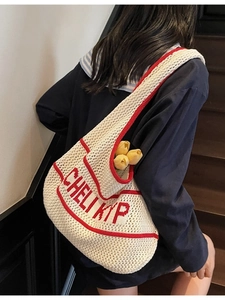 Knit tote bag with white crochet mesh and red letter embroidery on wooden stairs