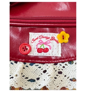 Detail of red patent leather tote with Sweet Cherry Garden embroidery and lace trim