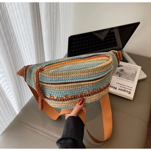 Detail of bohemian straw chest bag with colorful stripes and orange strap on a desk