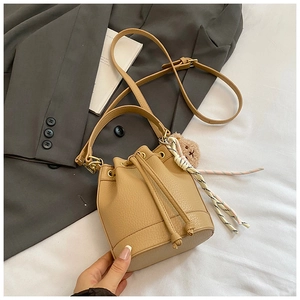 Detail of tan bucket bag with pebble leather texture, drawstring, and bear charm accessory